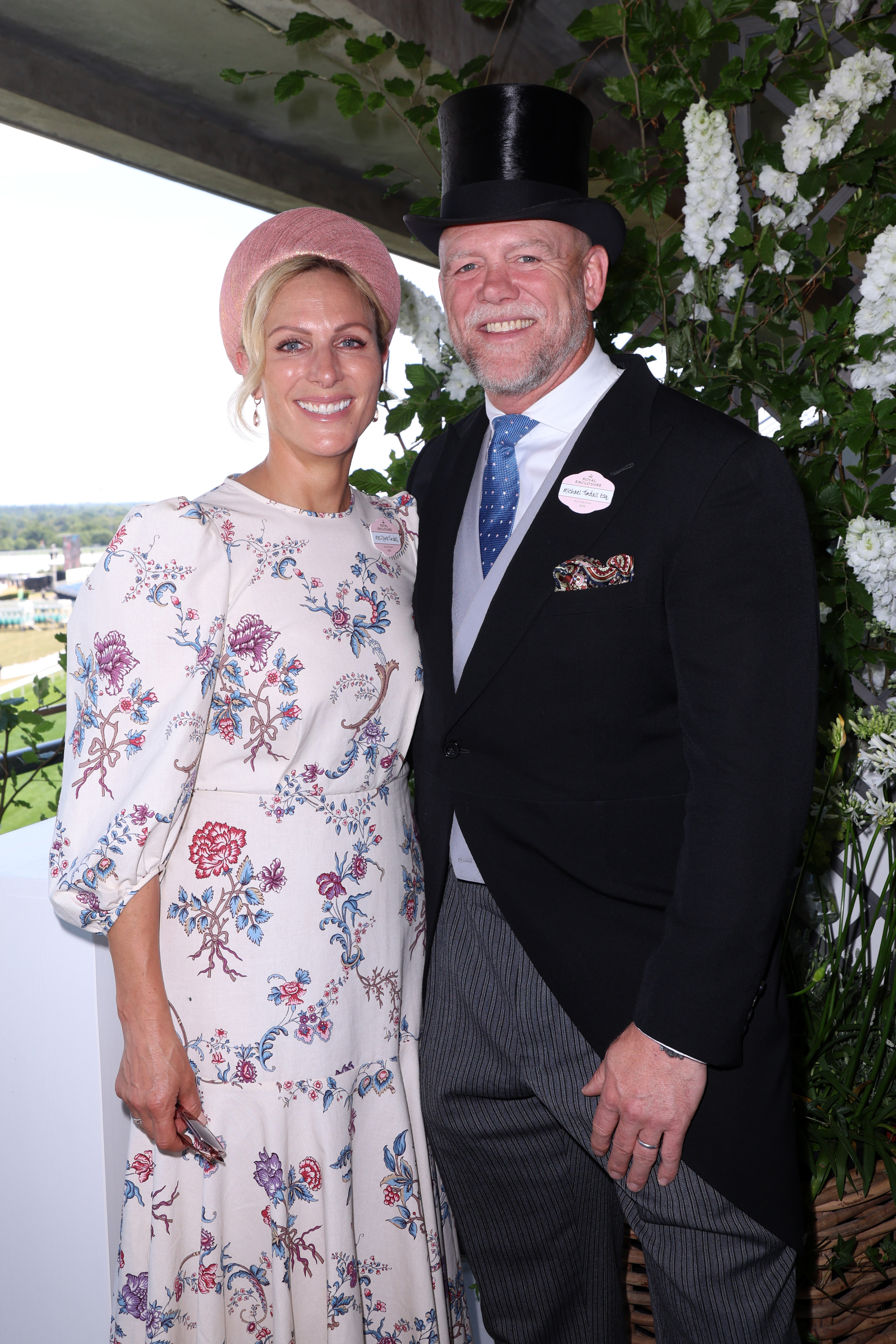 Zara Tindall wearing a white floral dress and pink headband standing with Mike Tindall, dressed in a top hat and suit