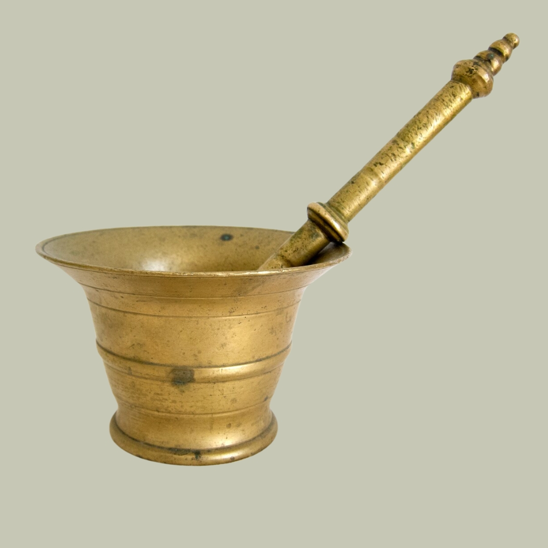 Antique early 1900s Spanish cast brass mortar with pestle against pale green background.