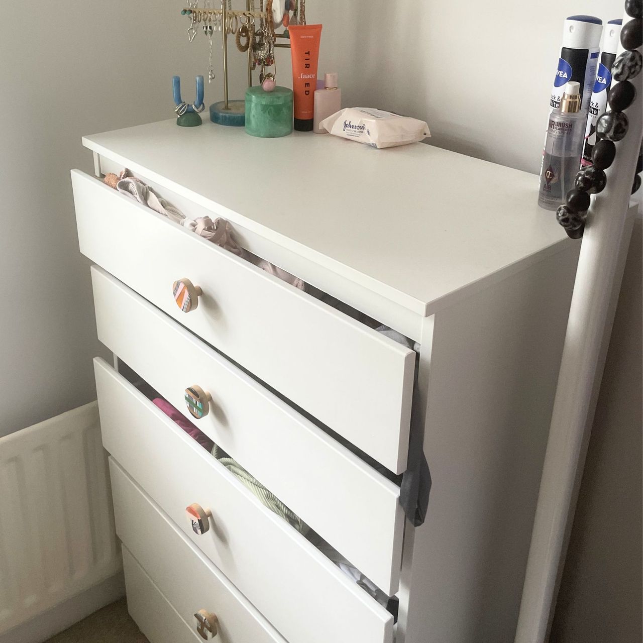 White chest of drawers with clothes spilling out of them in a white painted room