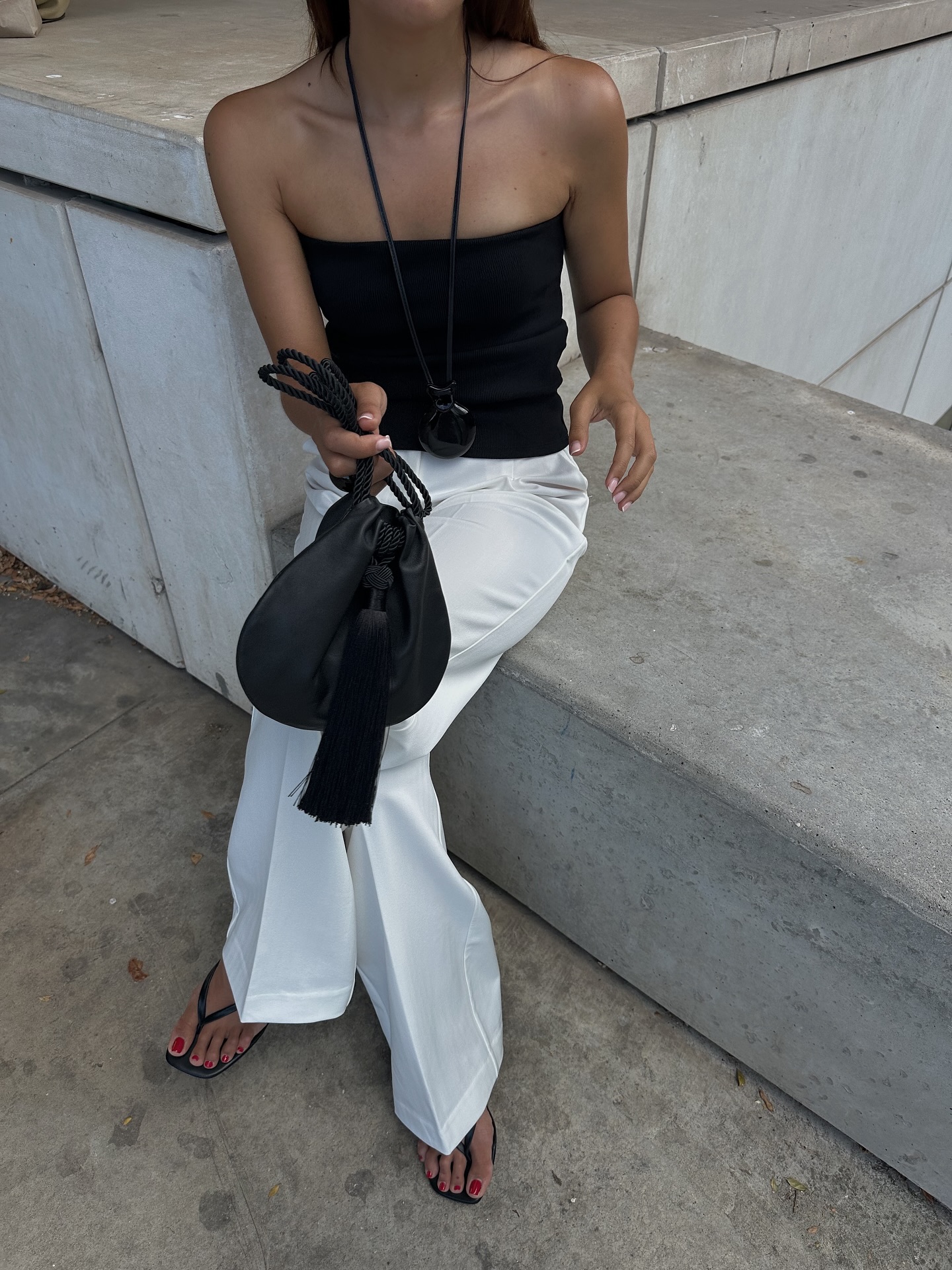 An image of @deborabrosa wearing a black strapless top with white trousers and a tassel bag.
