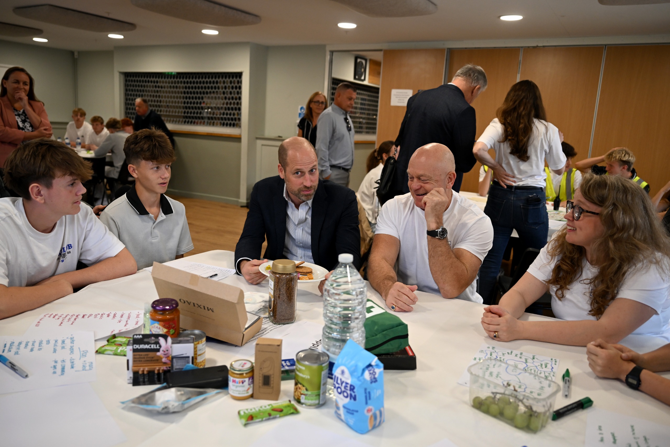 Prince William and Ross Kemp sitting at a table with students