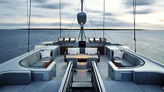 View of the upper deck of superyacht Vertigo featuring grey seats with white cushions and round tables. There is also a view of the ocean