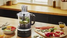 Slap chop vs food processor - a food processor on a kitchen counter, surrounded by vegetables.