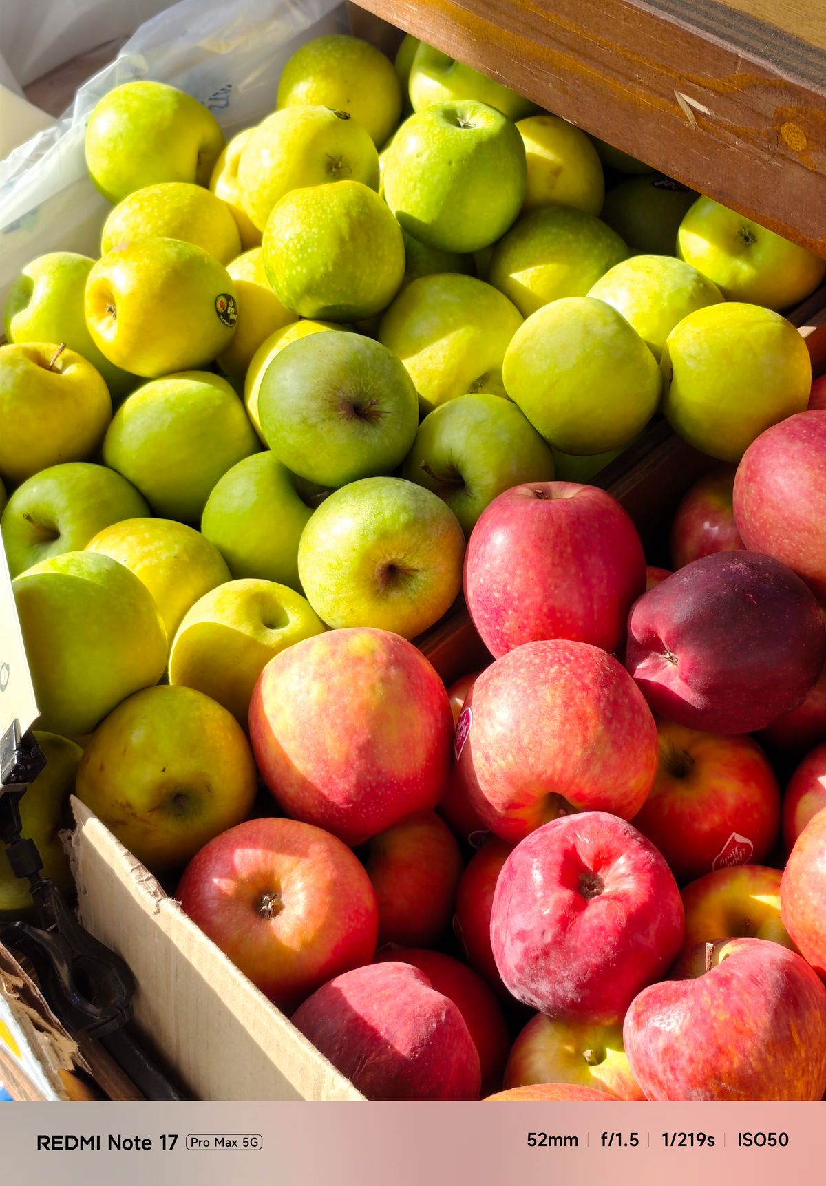Close-up of green and red apples displayed at an outdoor market stall in direct sunlight.