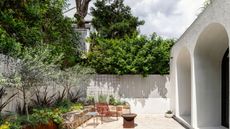 A garden with a patio chair and a firepit area. There are also plants placed all around with large hedges above the fences