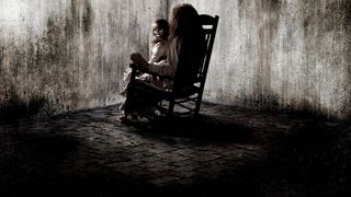 En tjej sitter i en gungstol med en docka i famnen och stirrar in i en smutsig stenvägg i The Conjuring