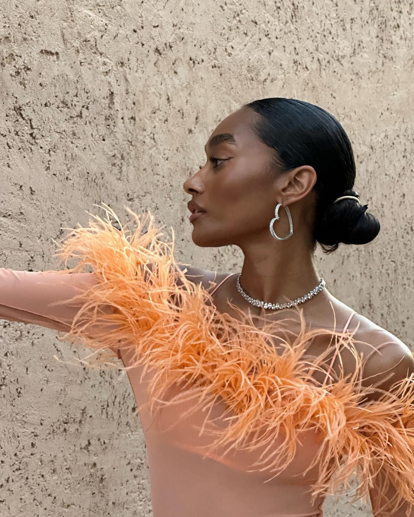 A woman wearing an orange feather dress with her hair slicked back into a low bun updo.