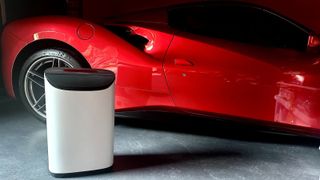 The Meaco DD8L dehumidifier in white on a concrete floor in a garage with a red super car behind it