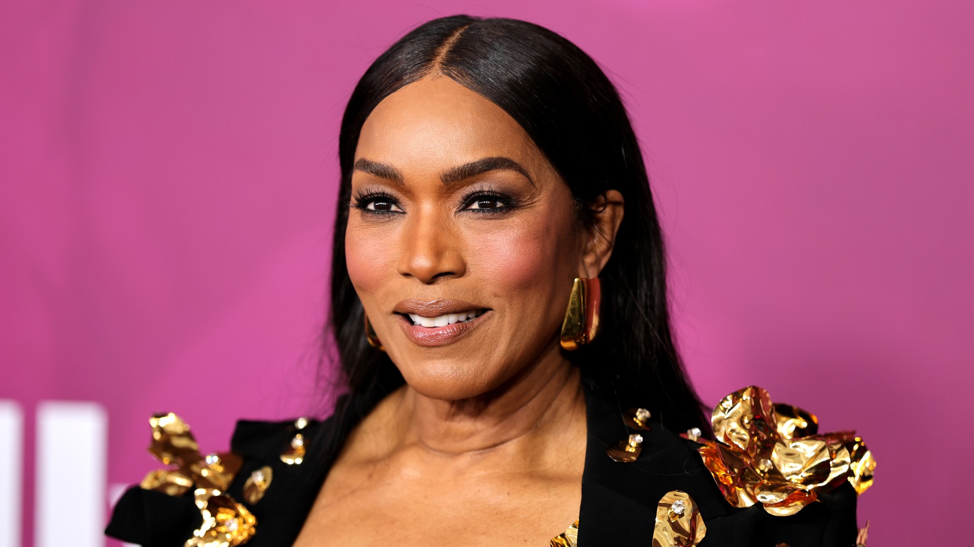 a black woman with dark hair poses in front of a pink background
