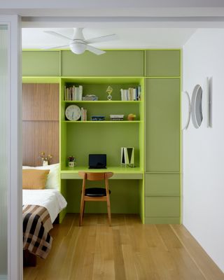 A bedroom designed in light wood, with the storage unit painted a bright shade of green