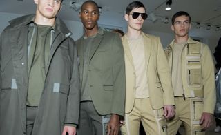 Four models wearing Calvin Klein clothing, two in olive colors and two in khaki colors