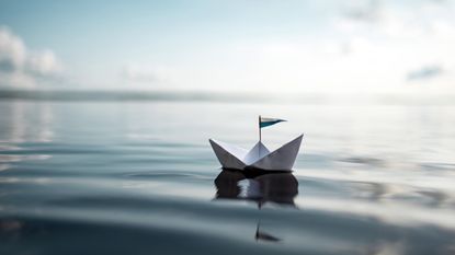 A paper boat sailing along a large body of water with subtle ripples