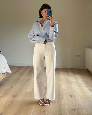 fashion influencer @smythsisters wearing a blue striped shirt, cream jeans, and white thong heels