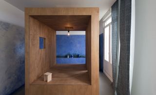 Meditation space, mahogany stained box takes centre-stage, blue and white swirl walls, white wall to the right with window and grey curtains, ceiling light