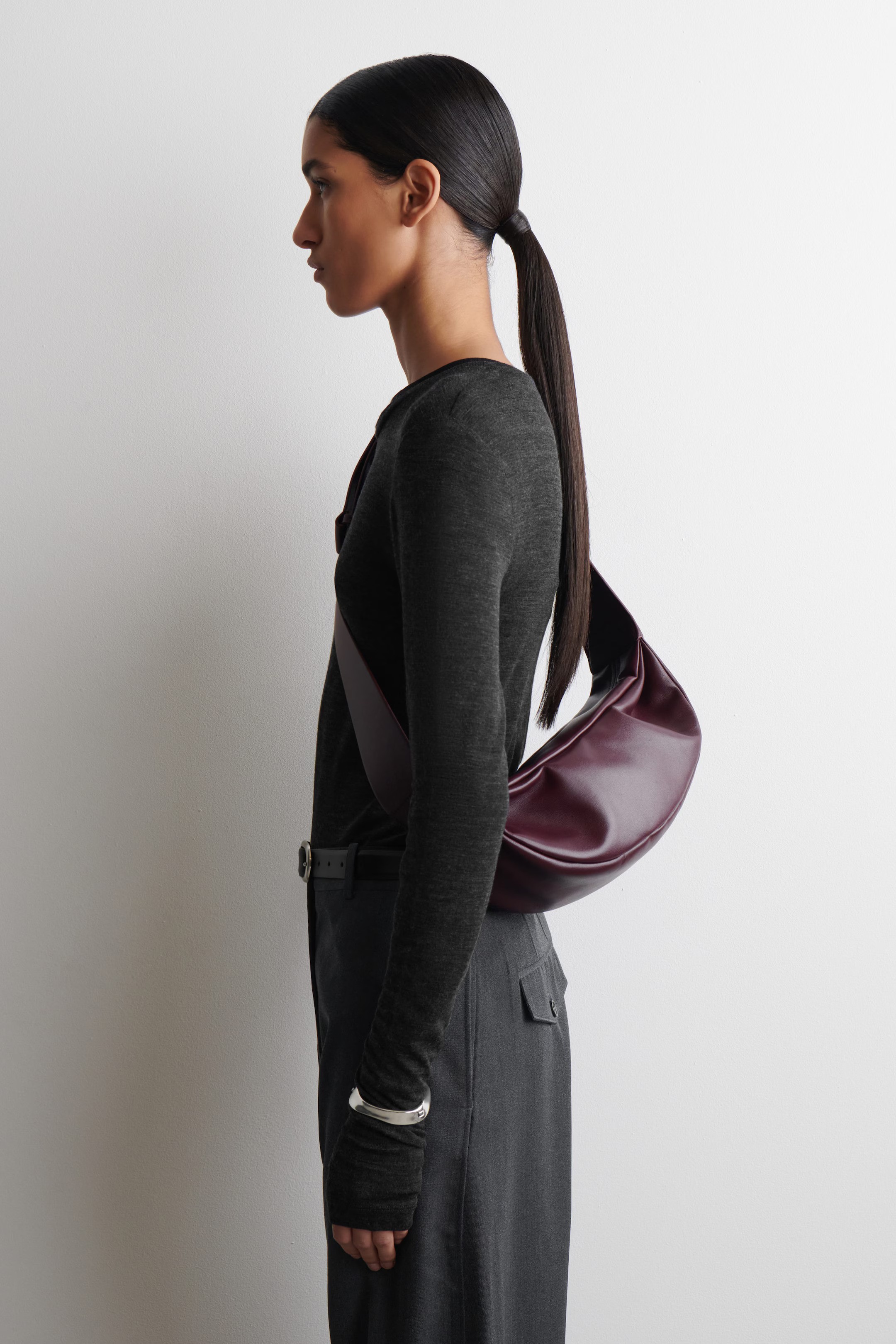 Model wears grey merino top, grey tailored trousers and cos burgundy swing bag