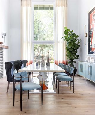 how to design a home that feels like you, dining room with white walls, hardwood floor, navy and pale blue velvet dining chairs, pale blue sideboard, gloss table, plant, candlesticks on table, cream ombre drapes