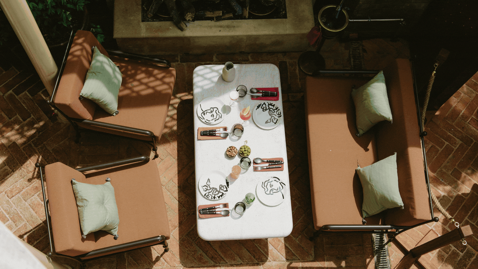 A rotating gif showcasing a restaurant terrace decorated with a mix of French cafe-style chairs, red and brown banquettes, thriving plants, and wrought iron furniture painted green.