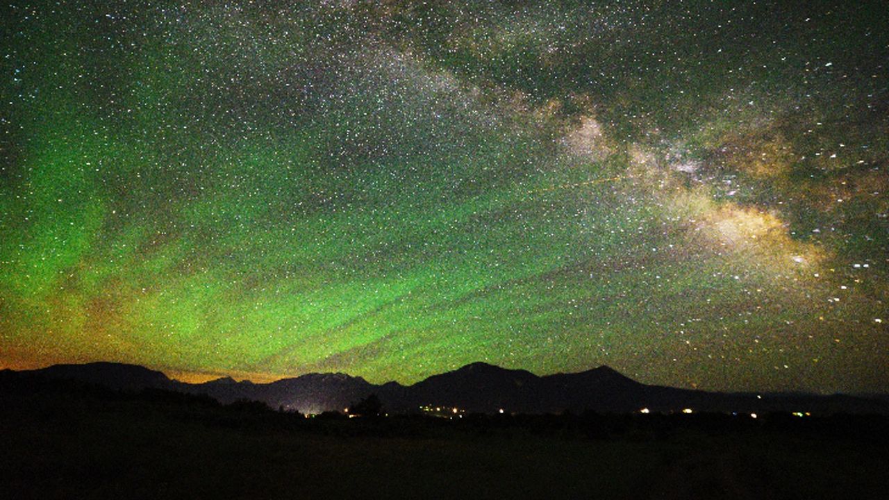 Green streaks of light shine in the night sky full of stars
