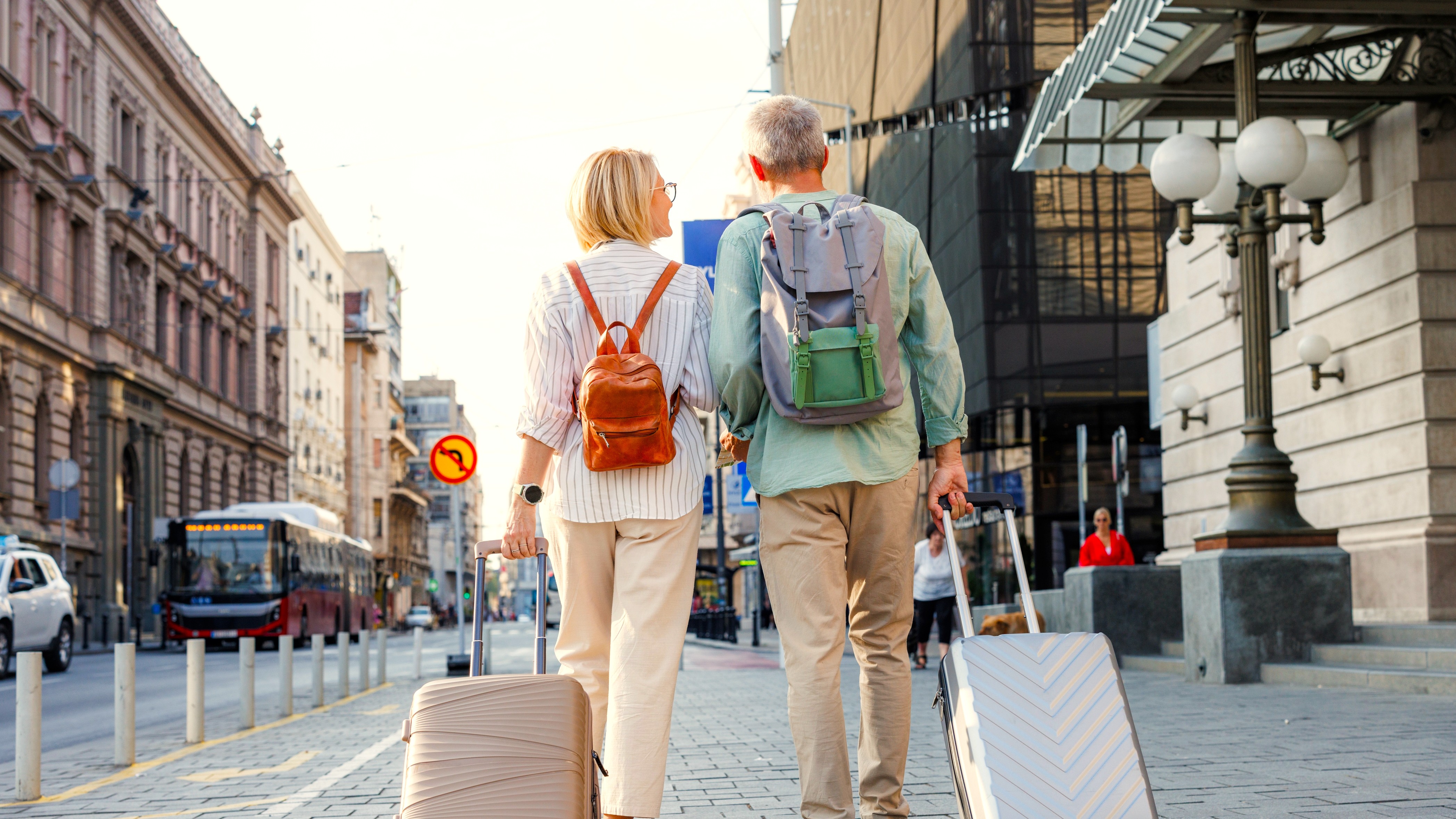 A senior couple walking down a street with luggage.