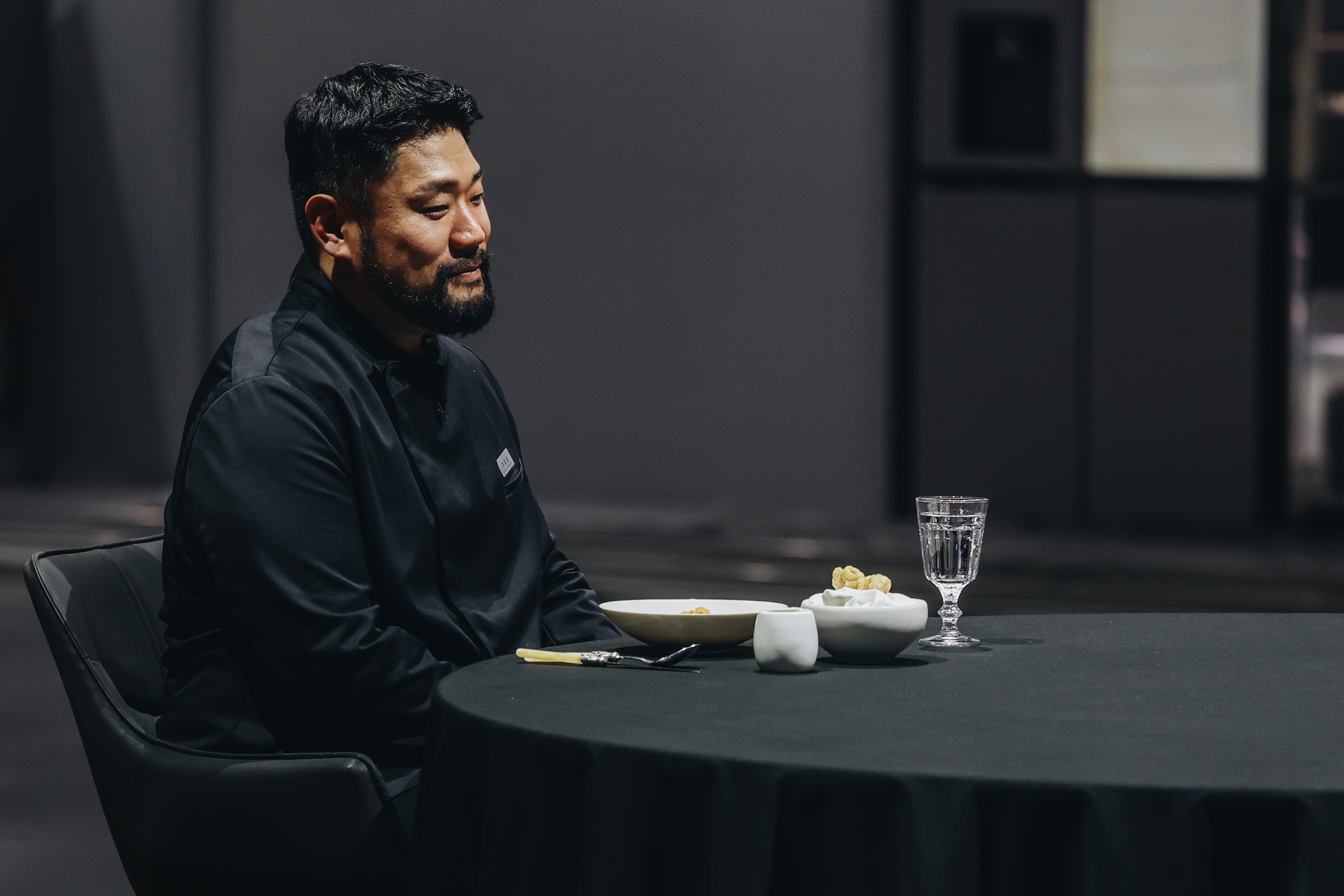 Chef Lee Ha-sung, nicknamed Culinary Monster, sits at a table with one plate setting, in Netflix's 'Culinary Class Wars.'