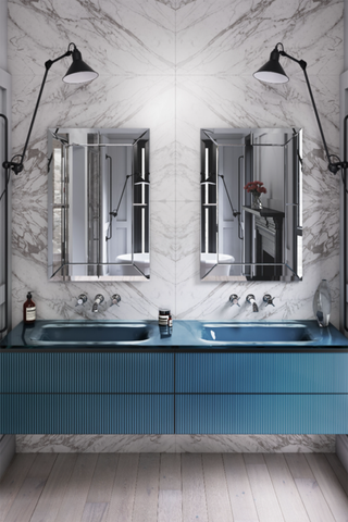 An example of bathroom layout ideas showing a blue double vanity unit in front of a marble wall with two mirrors on it