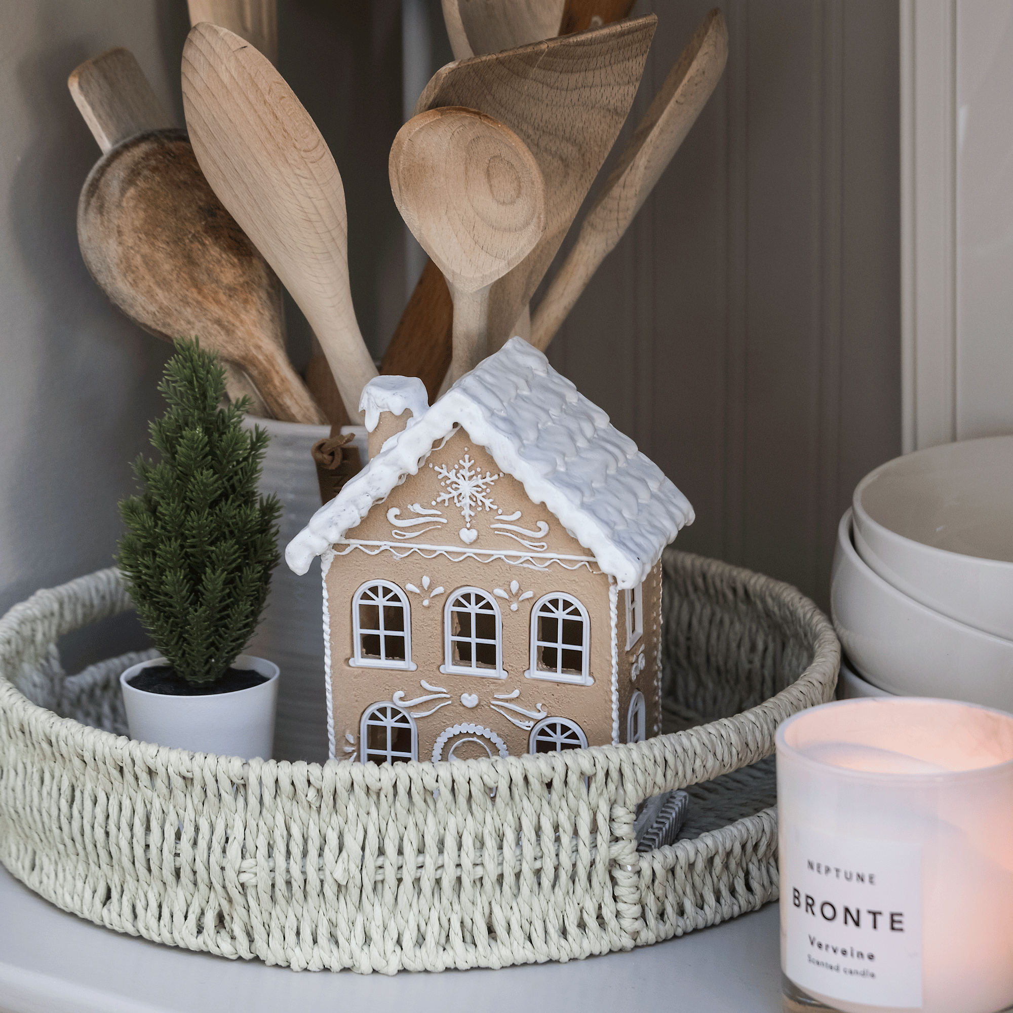 details of a wicker tray with a house tealight holder a pot of wooden spoons and a scented candle