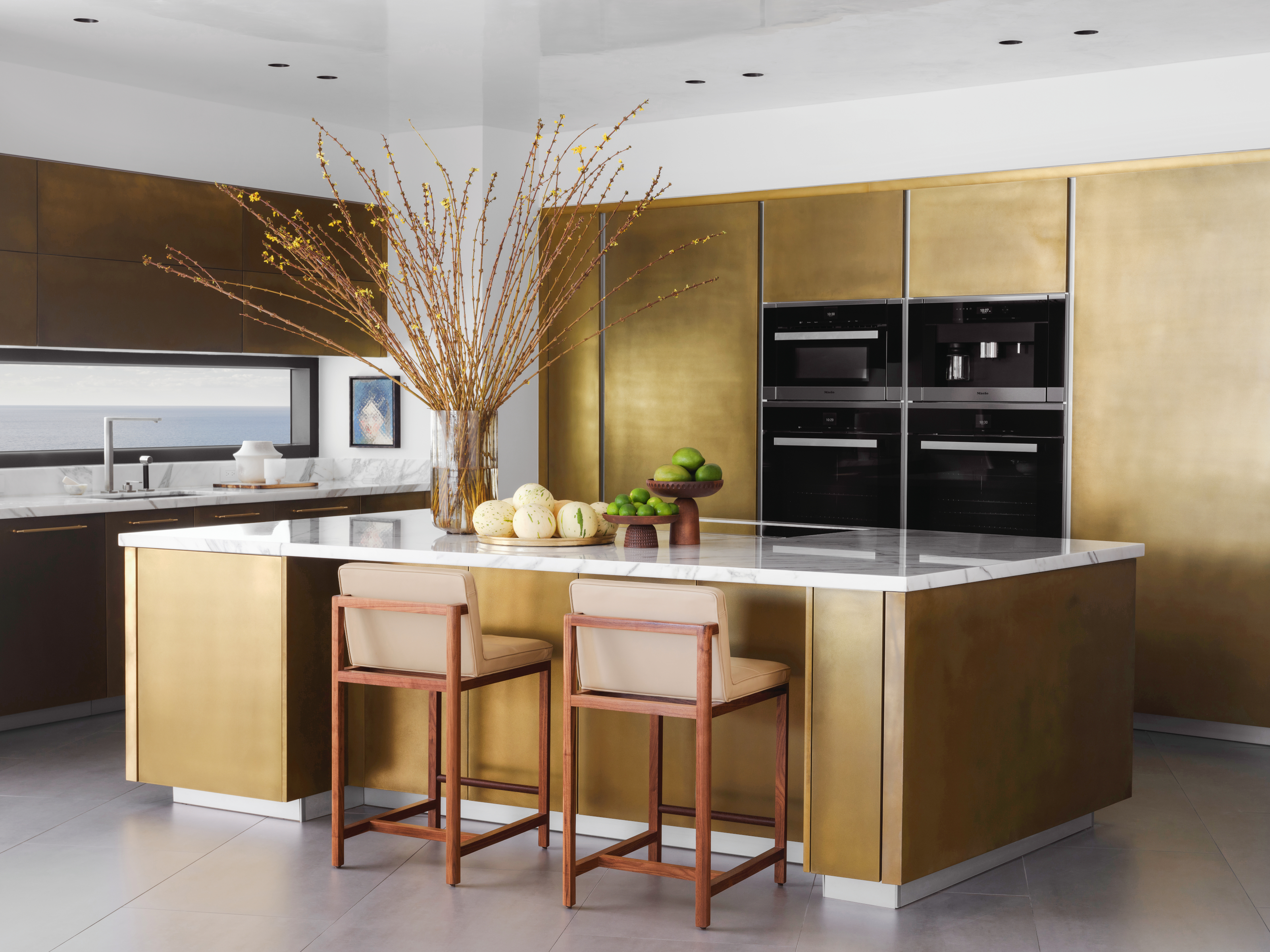 Brass metal lacquered kitchen and island with white worktops and wood framed bar stools