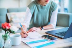 person looking at laptop and writing note as they deal with taxes