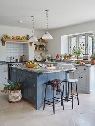 kitchen with blue freestanding island with marble worktops, white kitchen cabinetry with seating area plus bulter's sink and black stove