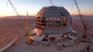 A giant domed building under construction on the top of a desert mountain.