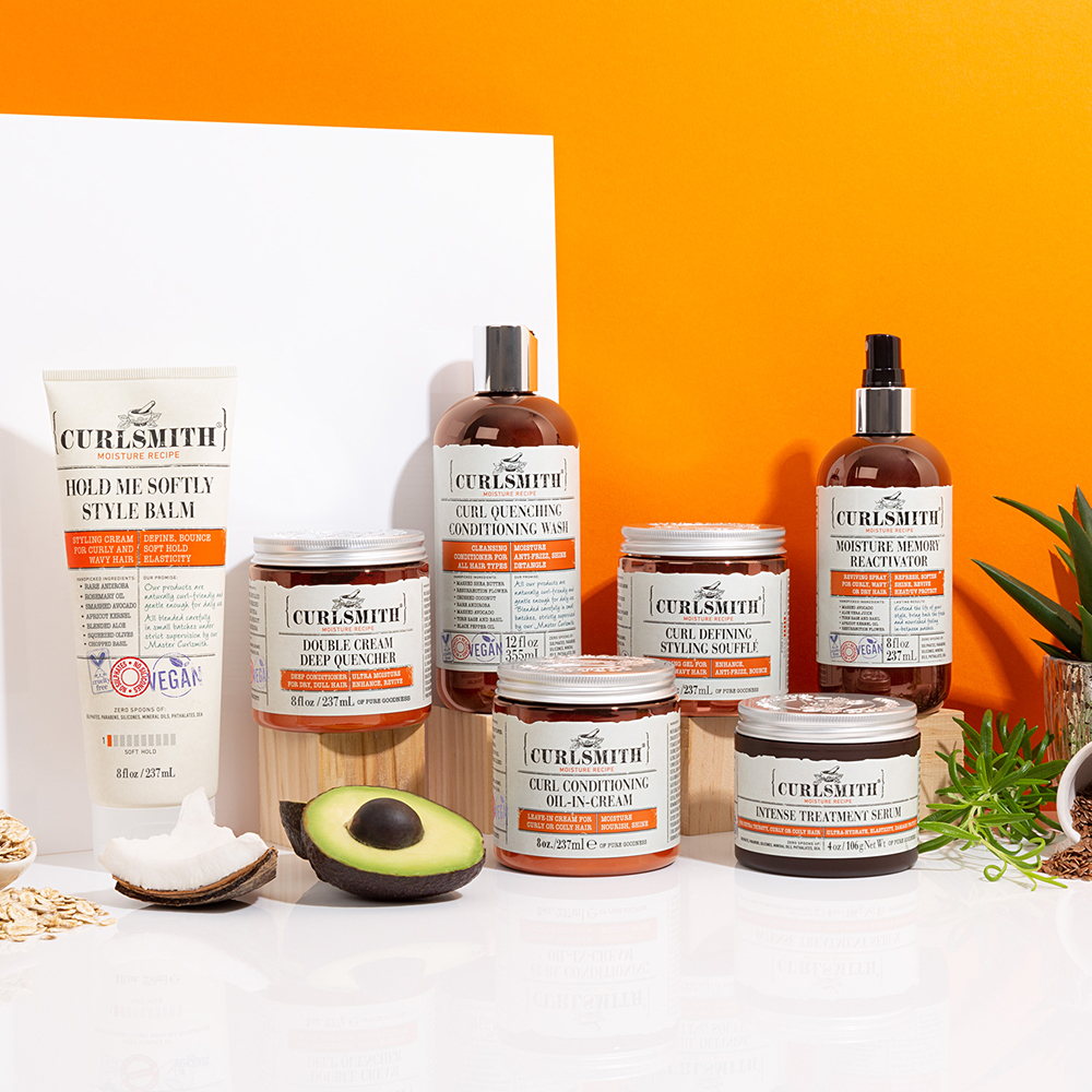 Selection of Curlsmith haircare products on an orange background with oats, coconut and avocados in the foreground