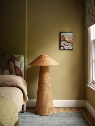 bedroom with pollen yellow walls, white skirtings, rattan floor lamp