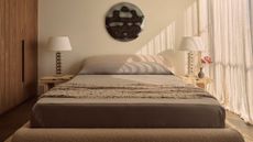 A white bedroom with a large bed in gray bedding, a textured coverlet, wood nightstands, matching textured lamps, a vase, and a round hammered chrome wall hanging