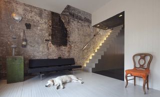 White dog sleeping on a light grey vertical lines wooden floor, with blac bench against a textured feature wall and next to a staircase.