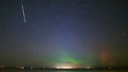 A streak of white light from a meteor graces the top left image of a blue and green starry night sky