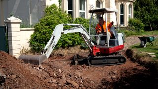 Mini digger digging up ground in front of period house