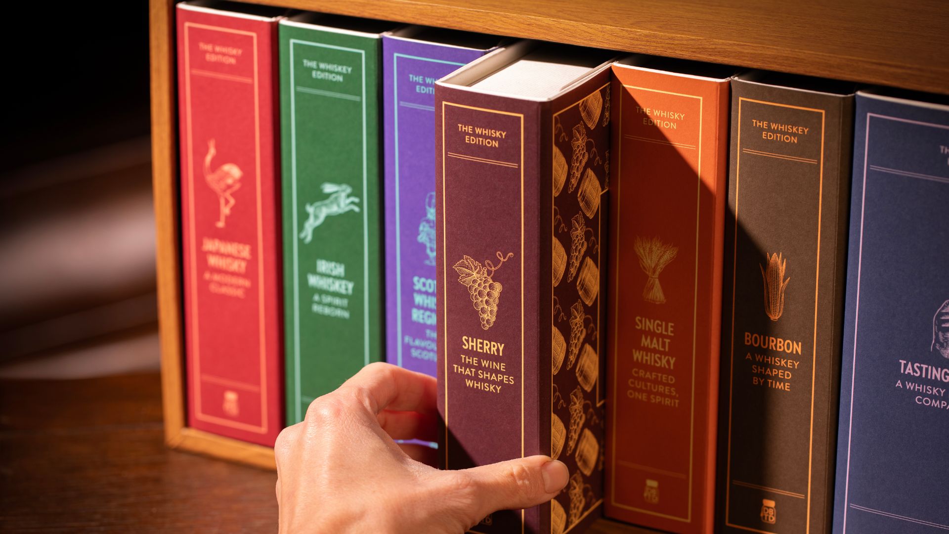 an image of the whisky library, show the six volumes in a wooden bookshelf, with someone reaching out to take one of the volumes , "Sherry", off the shelf