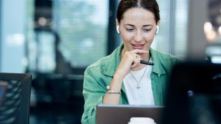 A woman working at her laptop, speaking to her headphones