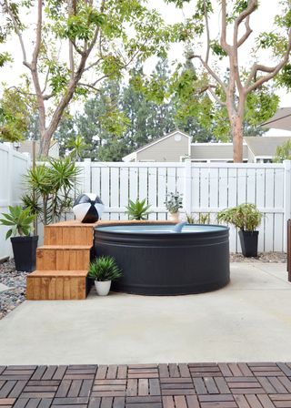 A round black pool with decked steps in a small concrete and decked backyard, demonstrating backyard ideas on a budget.