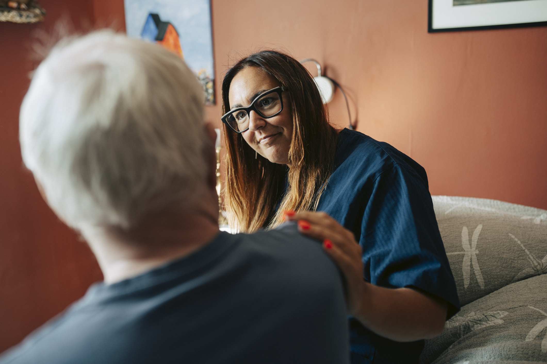 Carer wearing eyeglasses consoling senior man in nursing home