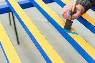 Timber pieces being painted blue and yellow