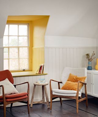 Living room with dark wooden floor and white walls, window frame painted yellow with two simple armchairs in front