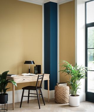corner of room with walls painted yellow, a blue column and small wooden desk and chair