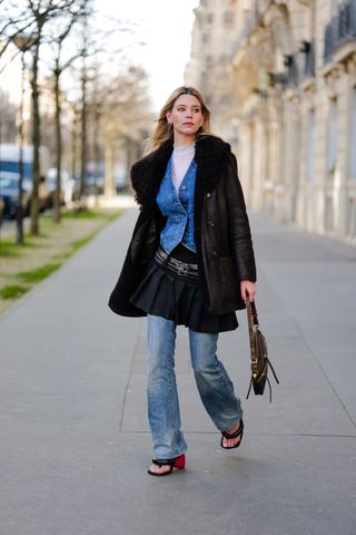 A woman a black mini skirt, jeans, a denim jacket, and two belts.
