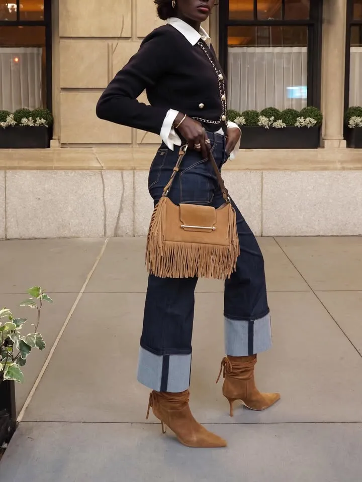 A woman wears slouchy suede boots with cuffed jeans and a fringe bag