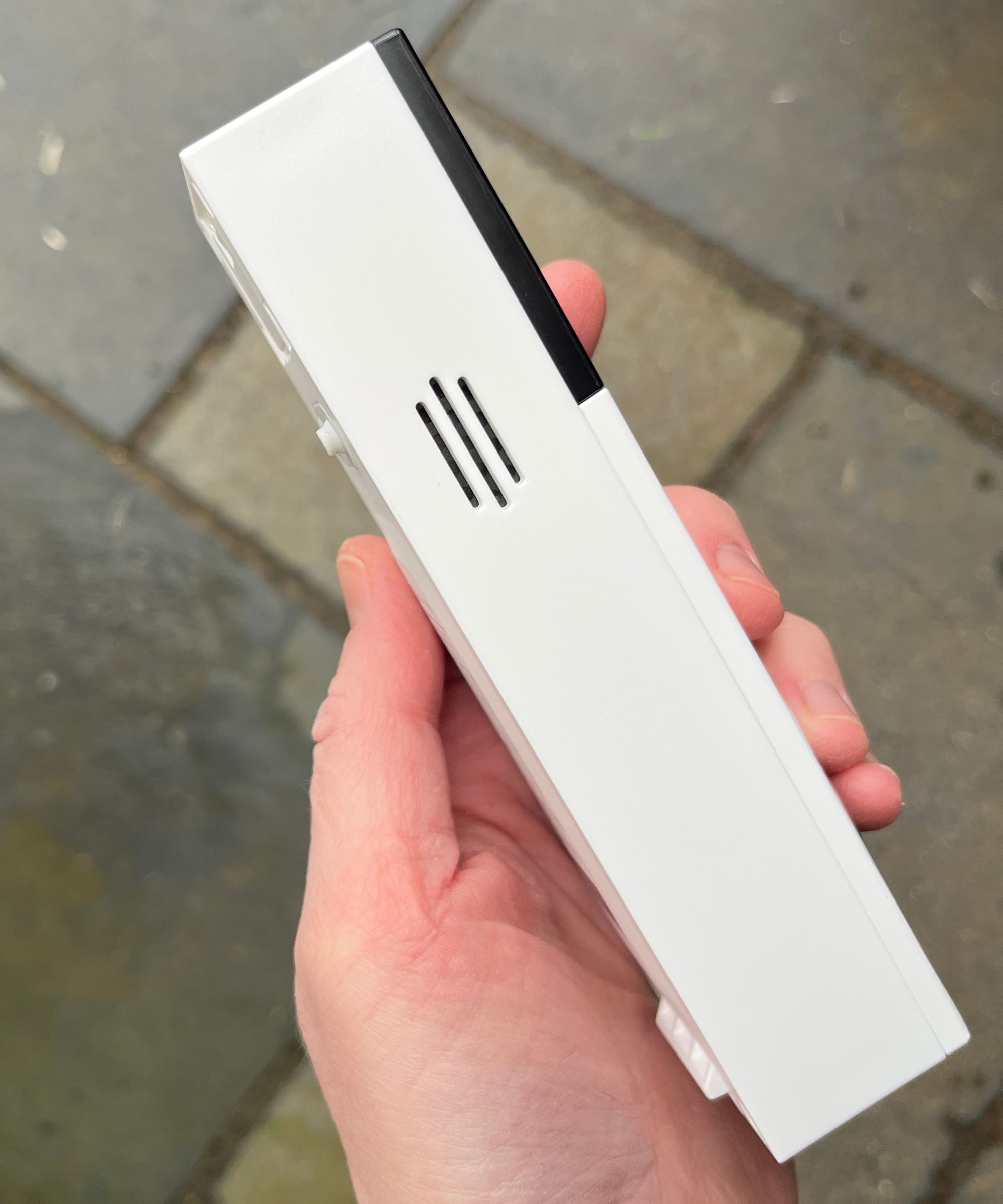 Hand holding the Tapo D210 Video Doorbell, showing the device's side, above tiled concrete floor.