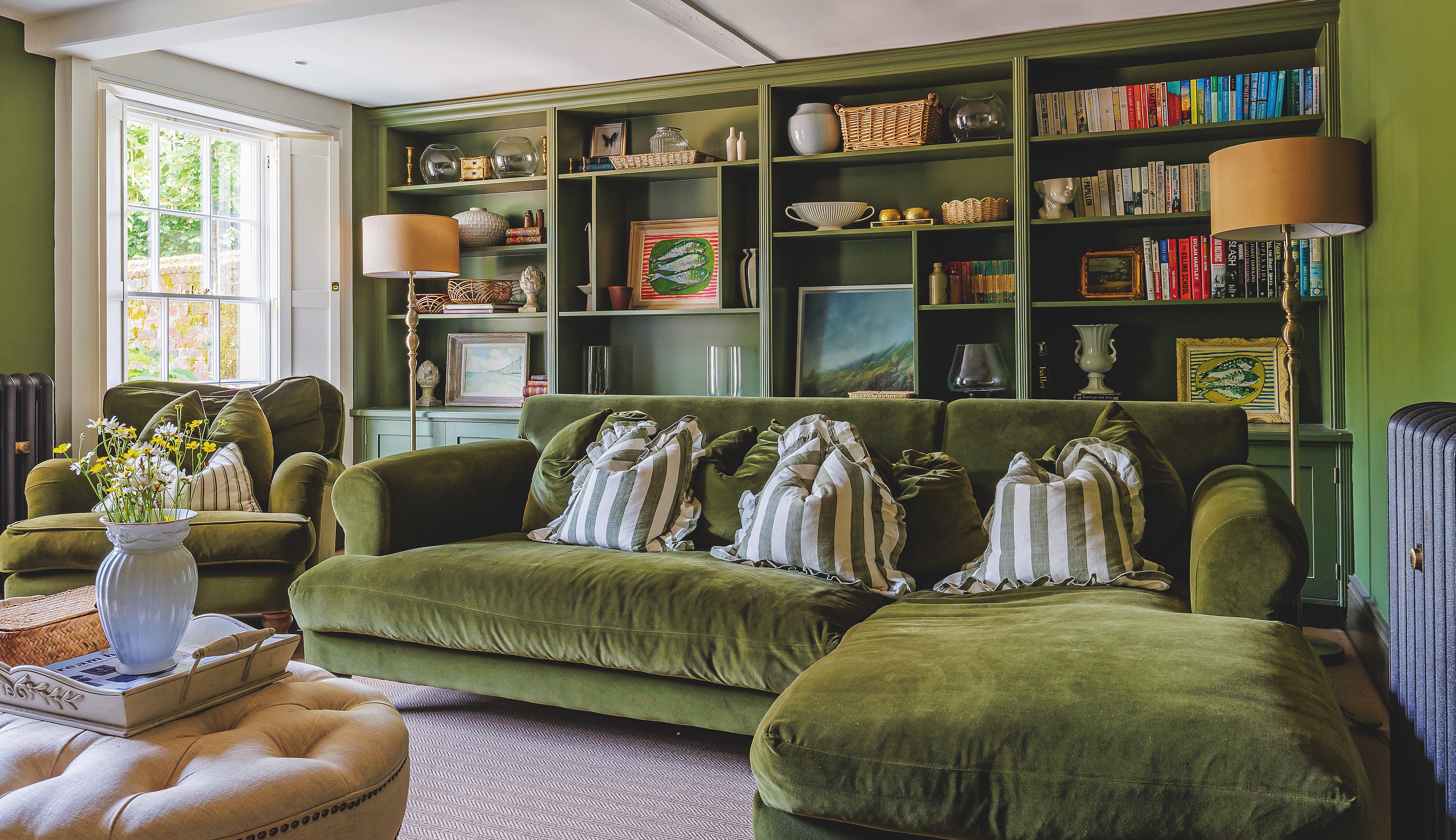 Sitting room with l-shaped green velvet sofa and fitted bookshelves