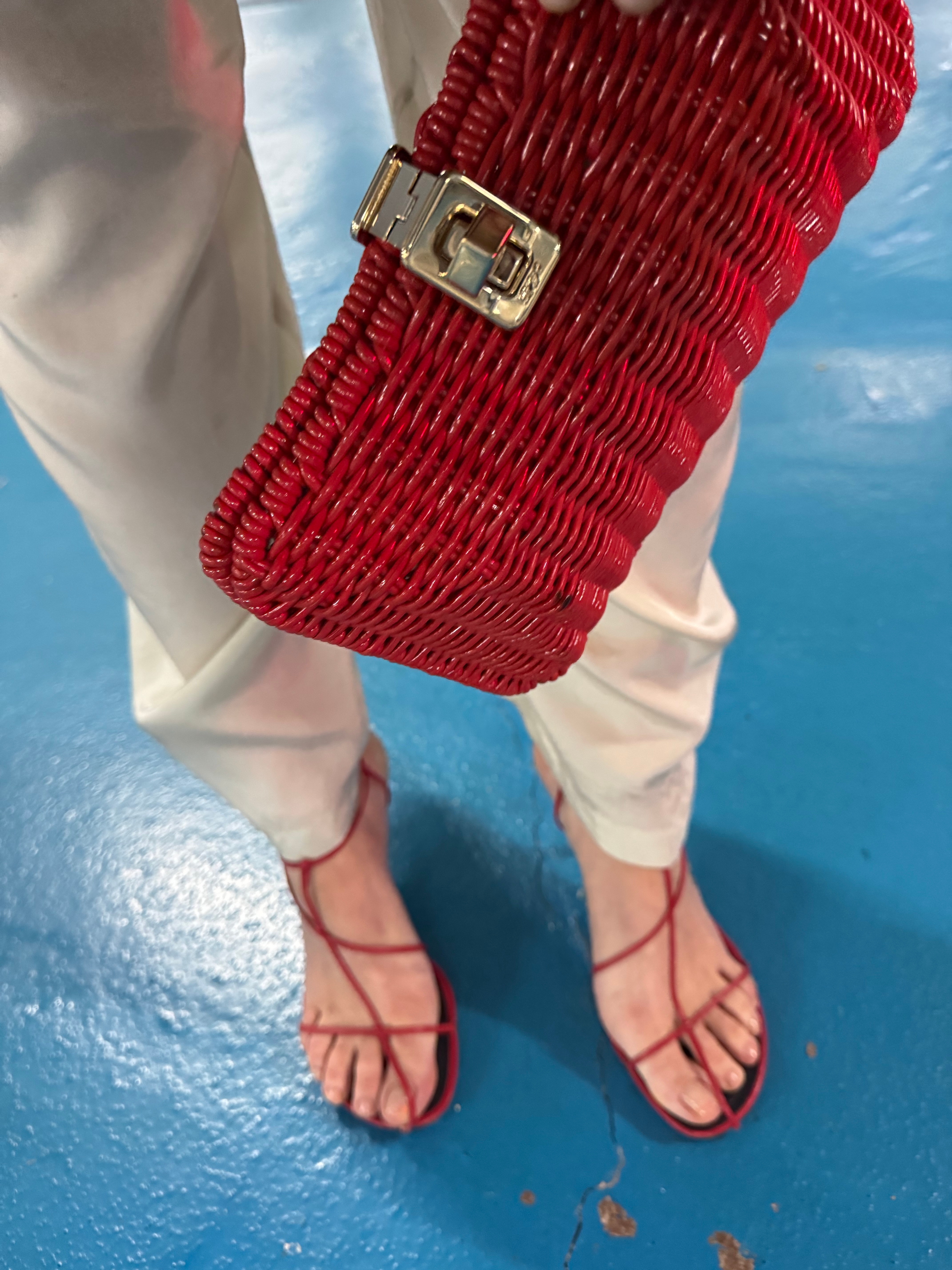 Blanca Miro wears red strappy sandals and a red woven clutch bag