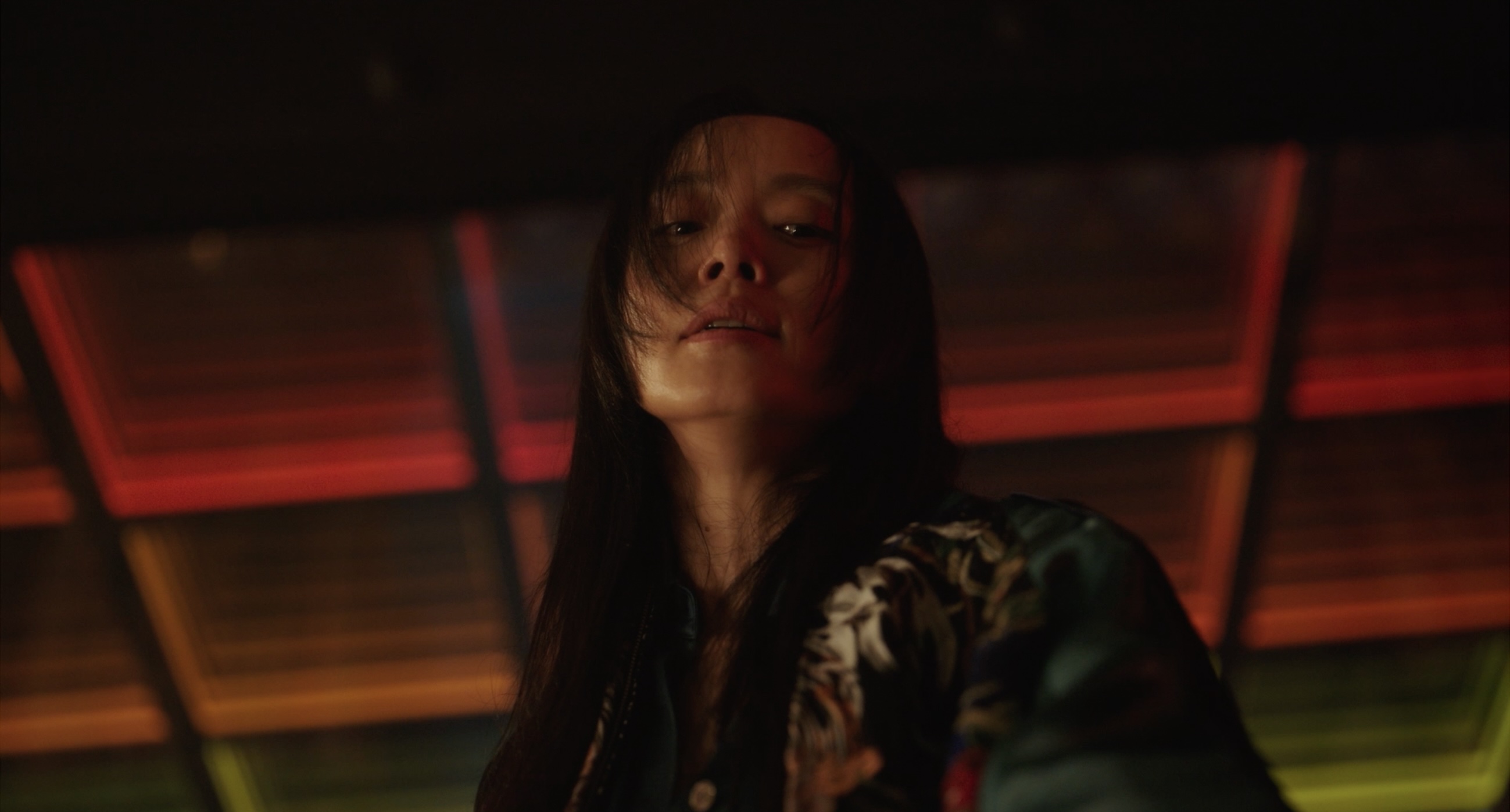 A woman (Jeon Do-yeon as Ha Soo-young) looks down while standing in a neon-lit room, in the Korean movie 'Revolver.'