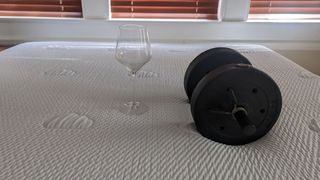 Puffy Lux Hybrid mattress with a weight resting on it, next to a wine glass